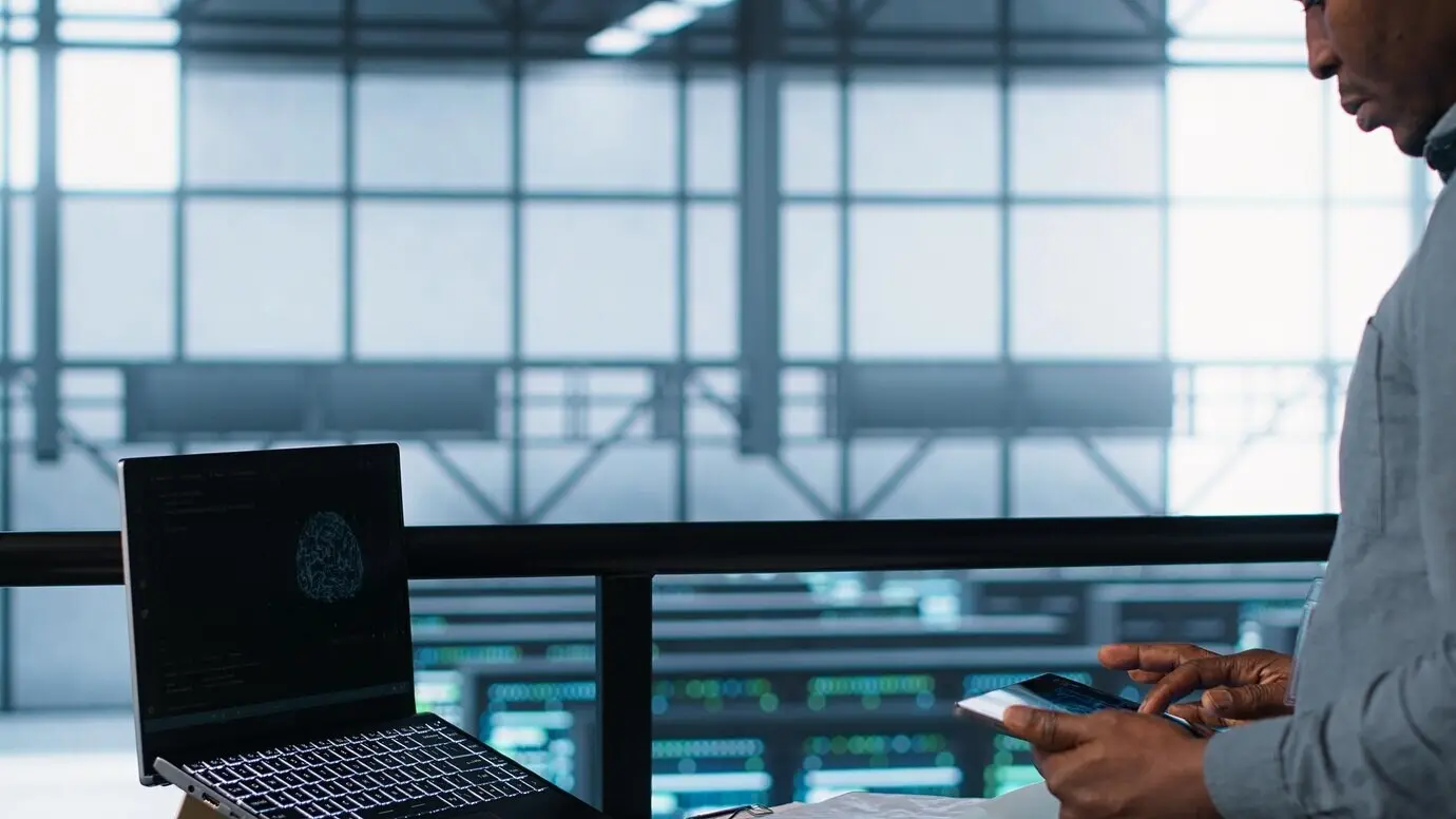Техник в дата-центре с ноутбуком и планшетом, интегрирующий технологию ИИ.